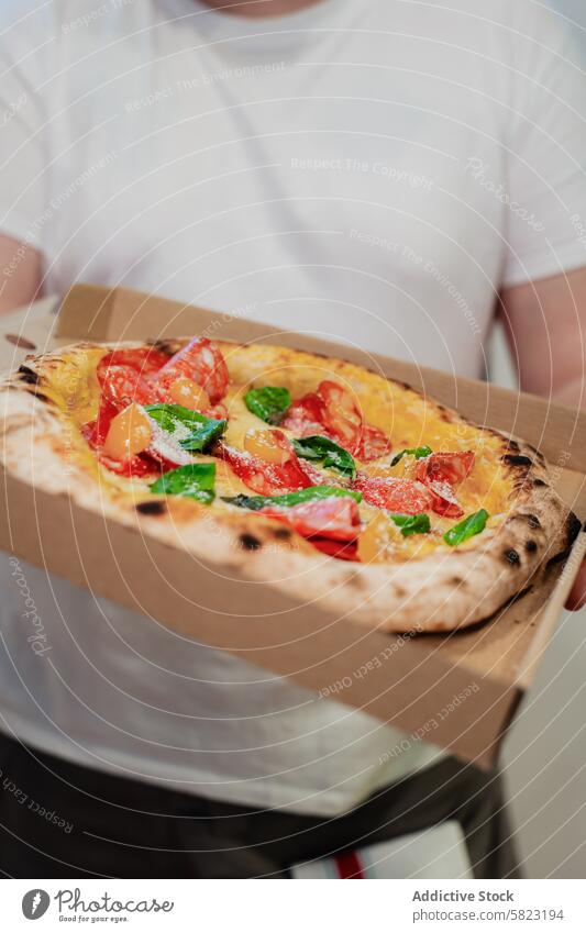 Freshly baked pizza in a delivery box held by a person cardboard food fresh holding anonymous faceless crop takeaway pizzeria italian meal cheese tomato basil