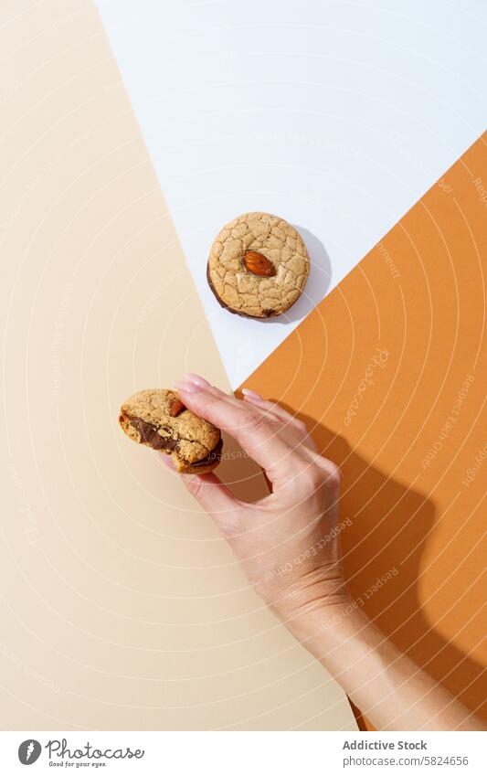 Hand picking a nut biscuit on a two-tone background hand homemade cookie cream orange surface snack sweet food dessert baked treat pastry person almond texture