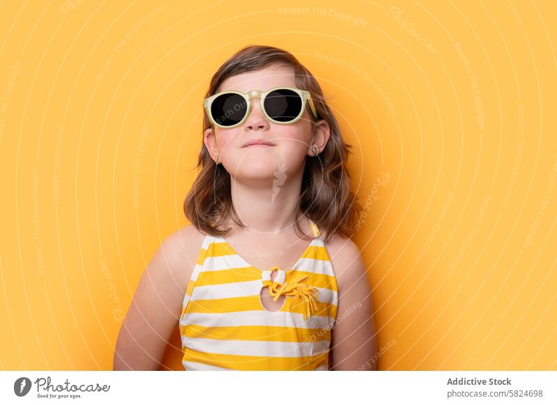 Young girl in sunglasses and striped swimsuit against yellow background smile vibrant fashion child summer style trendy young female oversized sunglasses lovely