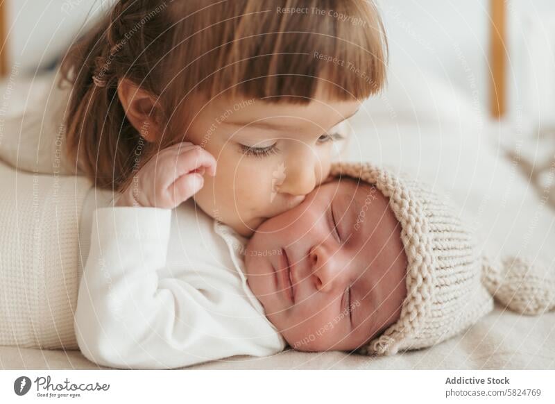 Toddler gently kissing a sleeping newborn baby toddler sibling gentle affection love cozy hat knitted heartwarming family infant child cute care tenderness