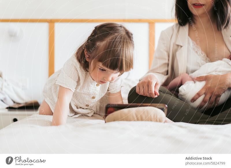 Tender moment of a toddler with her mother and newborn family gentle touch bed home cozy parent child baby bonding love affection sibling caring maternity