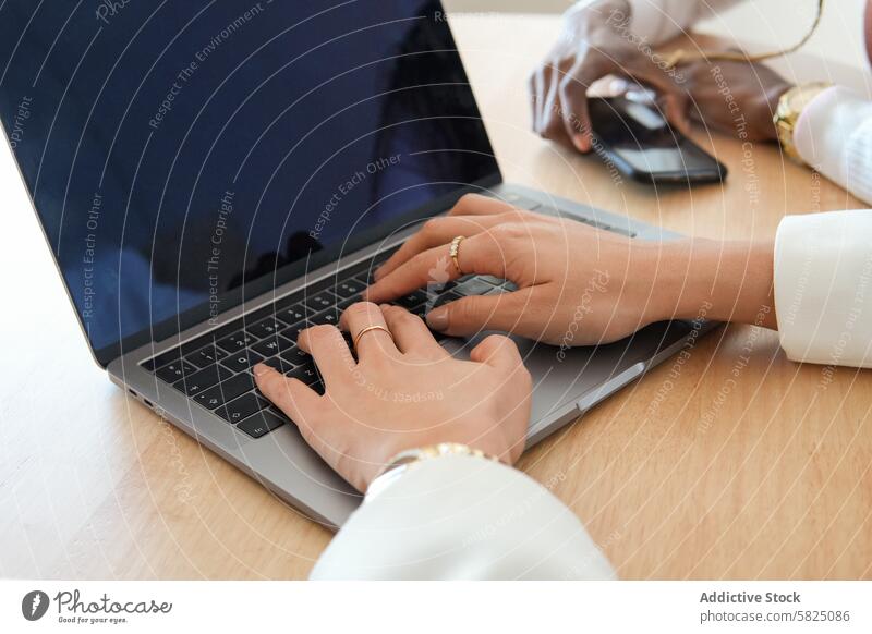 Two women collaborating in a modern home office setting woman work laptop smartphone desk wood productivity collaboration technology focus typing environment