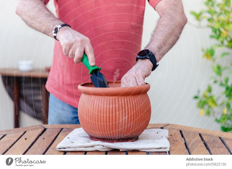 Man preparing a potted plant on a sunny backyard table man garden potting terracotta wooden outdoor trowel gardening hobby day soil focus activity nurturing