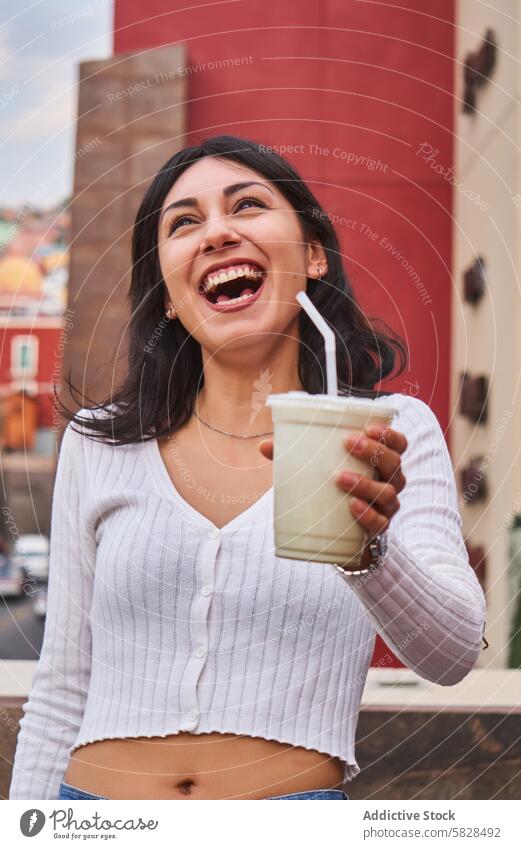 Joyful woman laughing and holding a drink outdoors beverage urban cheerful refreshing young female smile city lifestyle enjoyment leisure street energy carefree