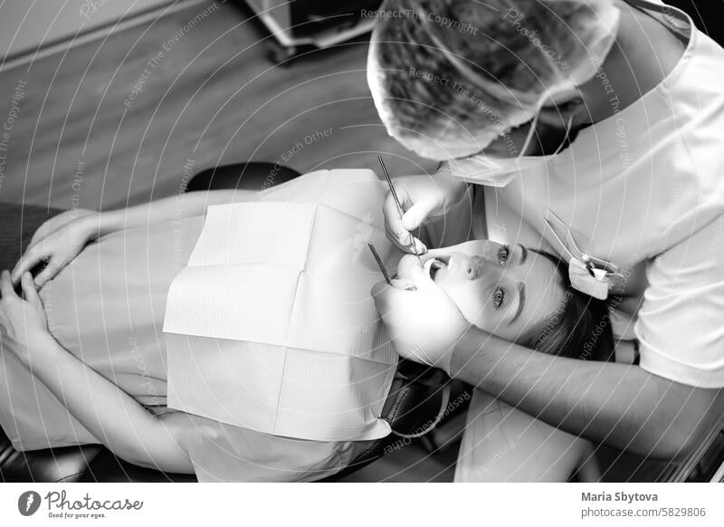 Dentist and patient at modern medical center. Doctor treats young woman teeth in hospital. Practitioner examines patient before orthodontists or prosthetics treatment. Black and white photo