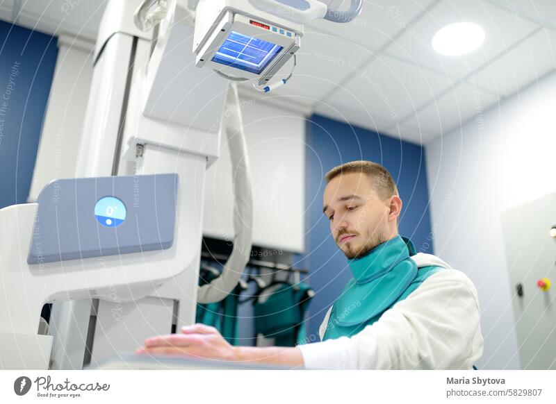 Young man having x-ray shot of broken hand in x-ray room in modern clinic. Patient wearing in protect lead apron radiologist crack bone joint arm fracture