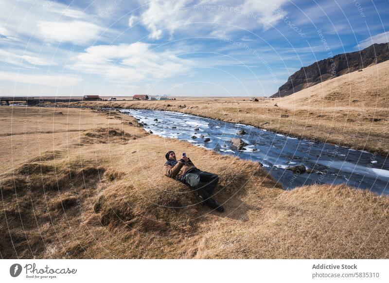 Relaxing by a stream in the grasslands of Iceland iceland landscape man reclining sky blue rugged outdoor tranquil peaceful nature serene leisure scenic travel