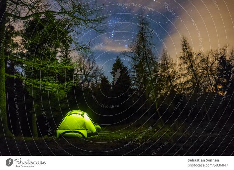 Green illuminated tent at the forest of the Vosges Mountains during winter under the stars of the night sky, Alsace, France trekking hiking travel recreation