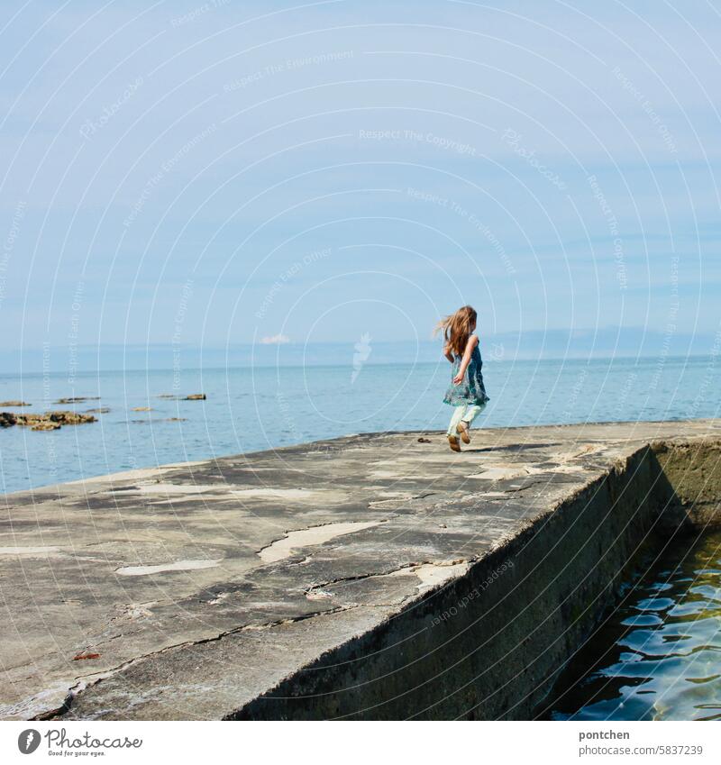 A child runs happily along a jetty by the sea, hair blowing in the wind. Child Happy Ocean vacation Footbridge holidays Dress Infancy Happiness Caucasian Life