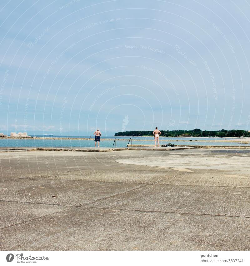 a man and a woman stand in the same posture with a view of the sea. a couple at a distance from each other. Posture Couple Woman Man Swimwear Ocean Stand