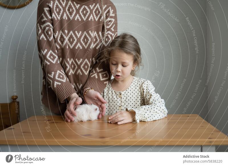 Tender moment with pet hamster at home mother daughter playing bonding wooden table indoors family gentle care animal fluffy white interaction focused nurturing