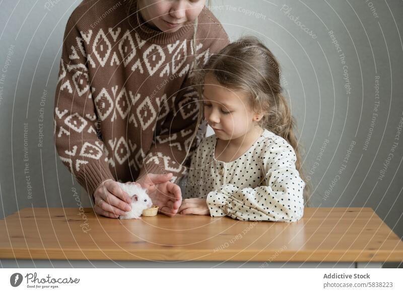 Tender moment with pet hamster at home mother daughter playing bonding wooden table indoors family gentle care animal fluffy white interaction focused nurturing