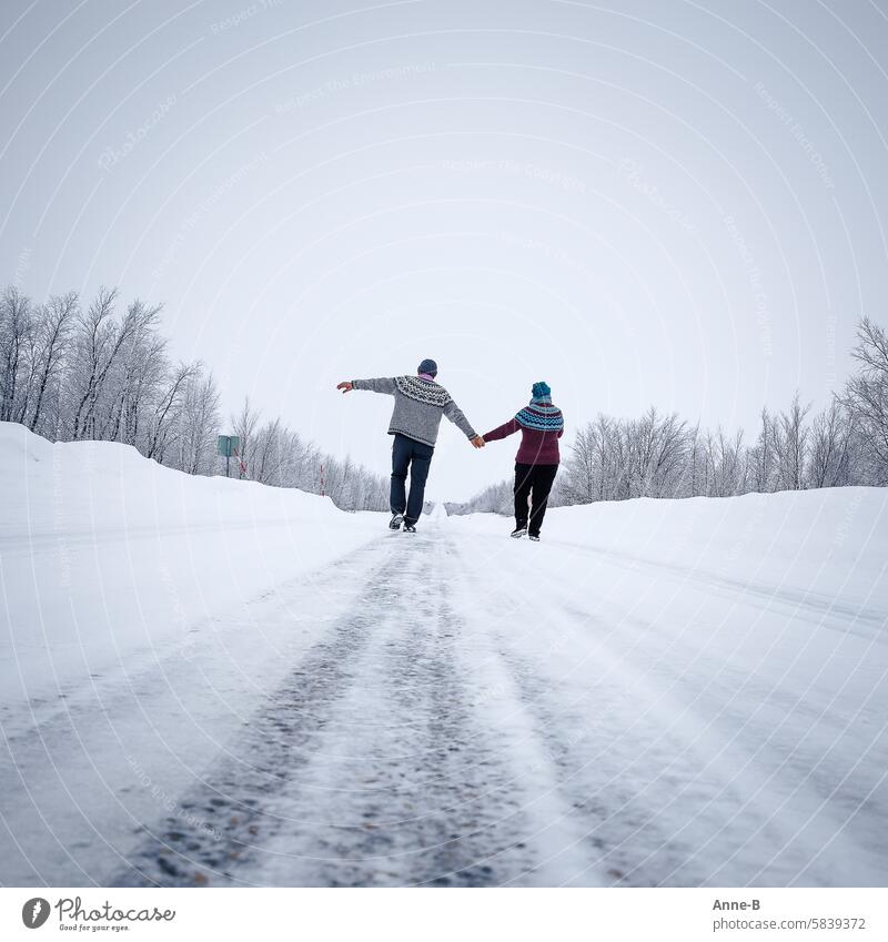 a cheerful couple strolls hand in hand on a street in the North Calotte in winter wearing beautiful thick home-knitted sweaters Knitted sweater Loneliness Love