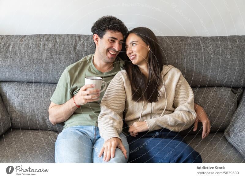 Happy couple smiling and enjoying coffee on couch sofa smile home interaction happiness sitting young comfortable casual warm indoor living room cup drink