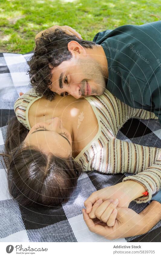 Romantic couple relaxing on a picnic blanket outdoors park romantic love young caress intimacy affection relationship holding hands gaze joy tranquility leisure