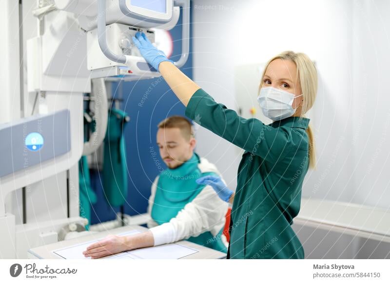 Young man having x-ray shot of broken hand in x ray room in modern clinic. Patient wearing in protect lead apron radiologist crack bone joint arm fracture