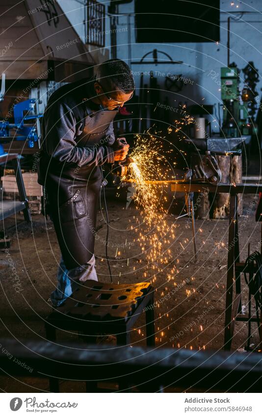 Artisan blacksmith working with metal in a workshop artisan male grinding sparks craft industry manual skilled labor protective gear apron tools equipment