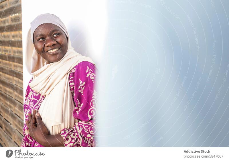 Smiling woman in colorful attire leaning against wall smile happiness joyous vibrant pattern culture diversity fabric cheerful african american positive