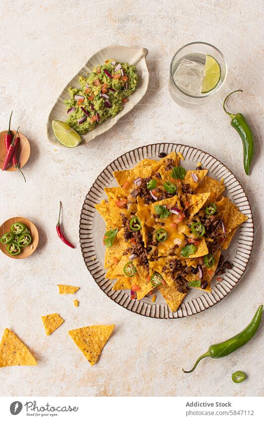 Top view of delicious nachos with guacamole on a textured background top view cheese ground meat jalapenos herbs lime drink rustic plate dish tortilla chips