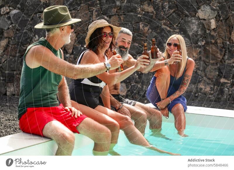 Group of senior friends enjoying beer by a pool swimwear toast bottle sunny day relaxing retirement enjoyment gathering casual leisure lifestyle together water