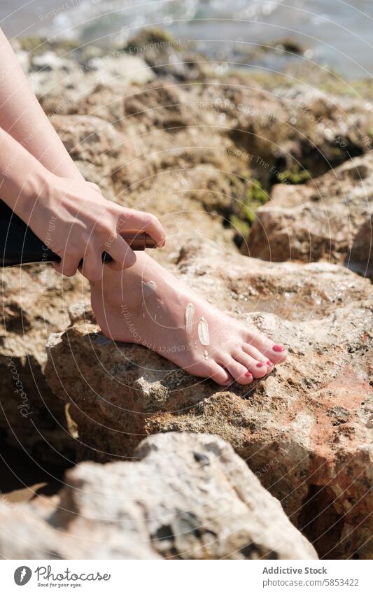 Person applying sunscreen on feet at a rocky beach skin protection sunbathing isolated sea summer health close-up application sunblock care safety leisure