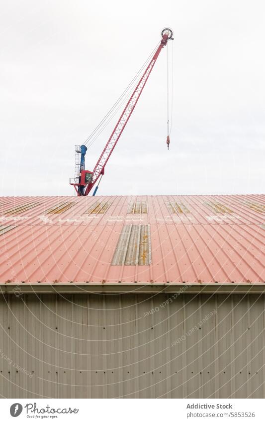 Large crane rising behind a metal roof structure sky construction industrial heavy lifting tall red weathered expansive capacity enhancement building project