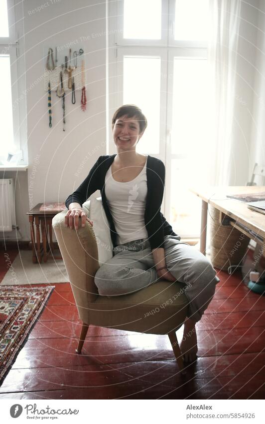 Young, slim student in sweatpants and top sits casually on an armchair at her desk and smiles at the camera Woman Young woman look pretty Slim Face Adults