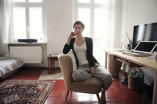 young, slim student in sweatpants and top sits casually on an armchair at her desk and looks into the camera Woman Young woman pretty Slim Face Adults naturally