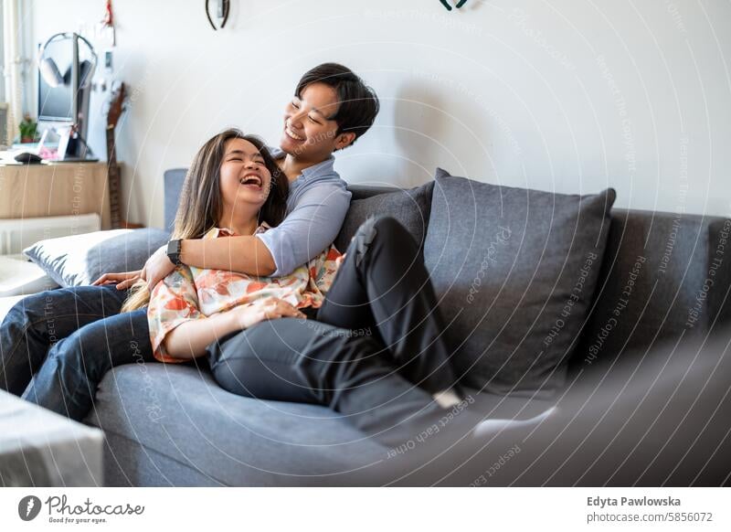 Smiling young couple relaxing on sofa asian real people fun enjoying young adult authentic cheerful confident female happy millennials natural portrait positive