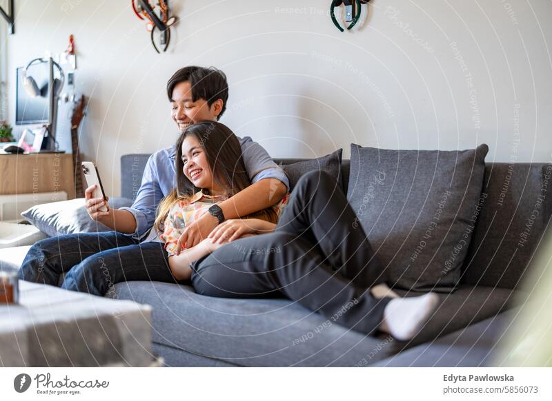 Smiling young couple relaxing on sofa asian real people fun enjoying young adult authentic cheerful confident female happy millennials natural portrait positive