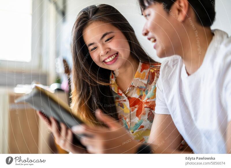 Happy young couple using digital tablet together on the sofa at home asian real people fun enjoying young adult authentic cheerful confident female happy