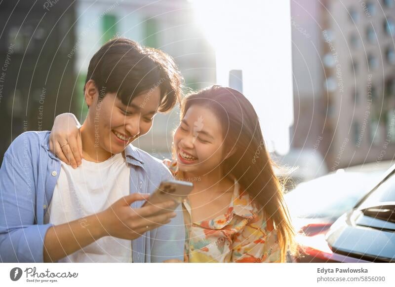 Smiling young couple using mobile phone in the city Asian real people fun enjoying young adult Authentic Cheerful Self-confident Woman Happy Joy Millennia