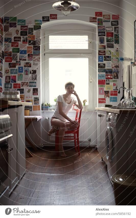 young, slim student sits in underwear in her kitchen on a red chair and looks into the camera - backlit shot Young woman Woman Student Kitchen Underwear