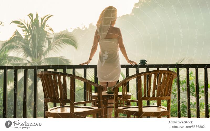 Woman enjoying morning on tropical balcony woman landscape serene coffee towel wooden table overlooking lush cup nature outdoor leisure relaxation peaceful