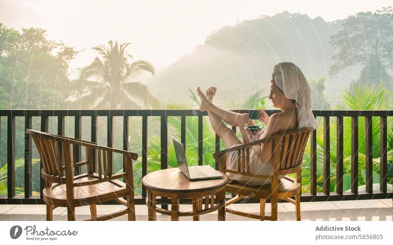 Woman relaxing with coffee and laptop on tropical balcony woman morning serene towel scenic landscape lush misty relaxation leisure work remote outdoor chair