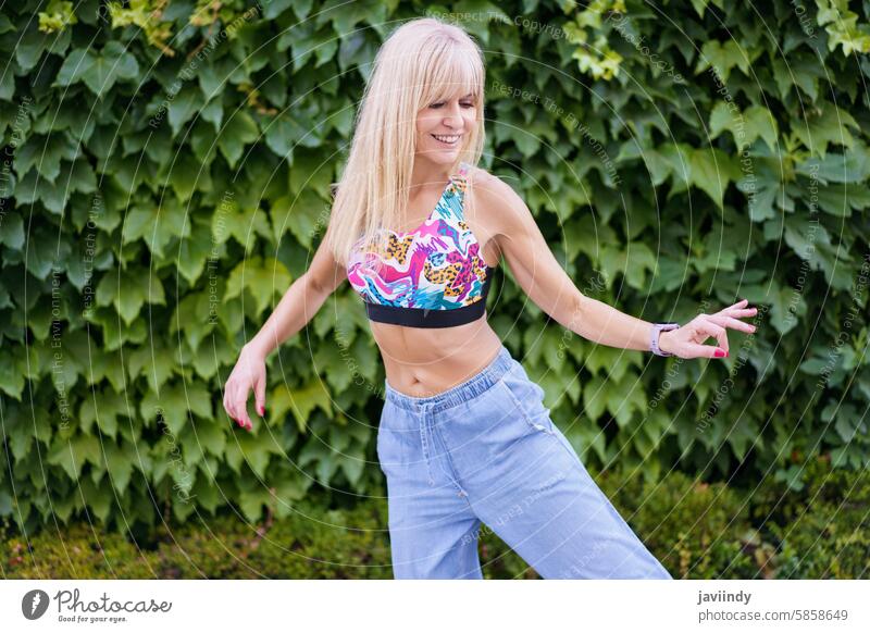 Woman expressing herself through dance next to an urban garden blonde cute young woman expression happy joyful energetic movement smiling freestyle outdoors