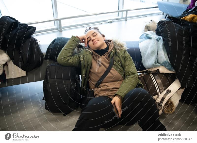 Woman resting at airport during travel woman napping luggage bench tired waiting transit passenger coat backpack sleep layover journey trip commuter tourist