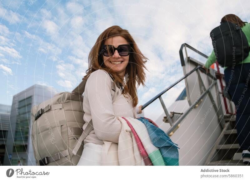 Smiling woman with backpack climbing stairs of a plane during travel smiling sunglasses outdoor adventure leisure joy happiness ascending sunny cheerful