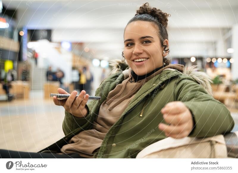 Smiling woman using smartphone in busy indoor area smiling blurred background crowd hand holding technology communication casual jacket young adult happiness