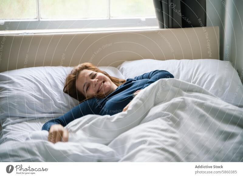 Morning joy of a woman relaxing in bed smile bedroom comfort cozy daylight window morning sheets pillow restful wellbeing happiness tranquility home alone