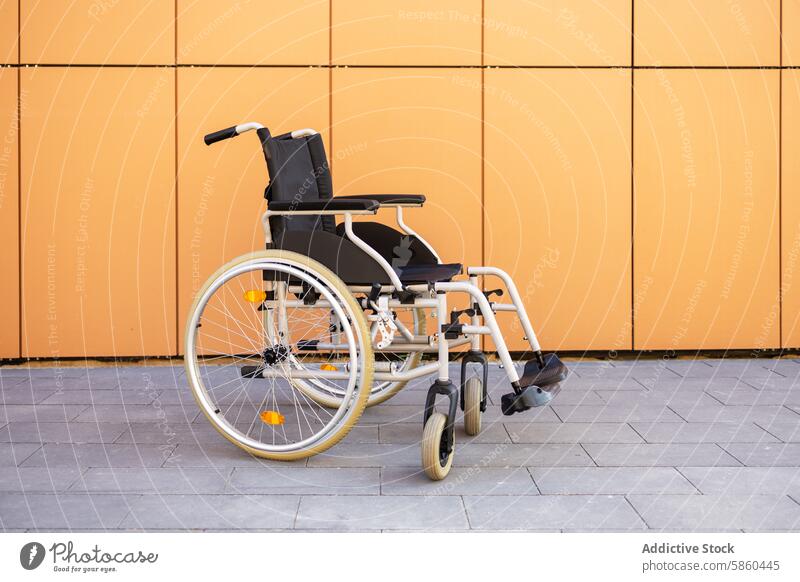 Modern wheelchair against orange wall accessibility mobility healthcare medical equipment disability assistive technology modern bright empty outdoor pavement