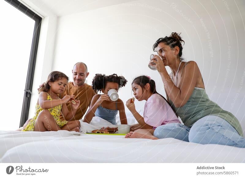 Multiethnic family enjoying breakfast in bed together multiethnic children morning eating drinking happy cozy bedroom sunlight meal muffin cup casual comfort