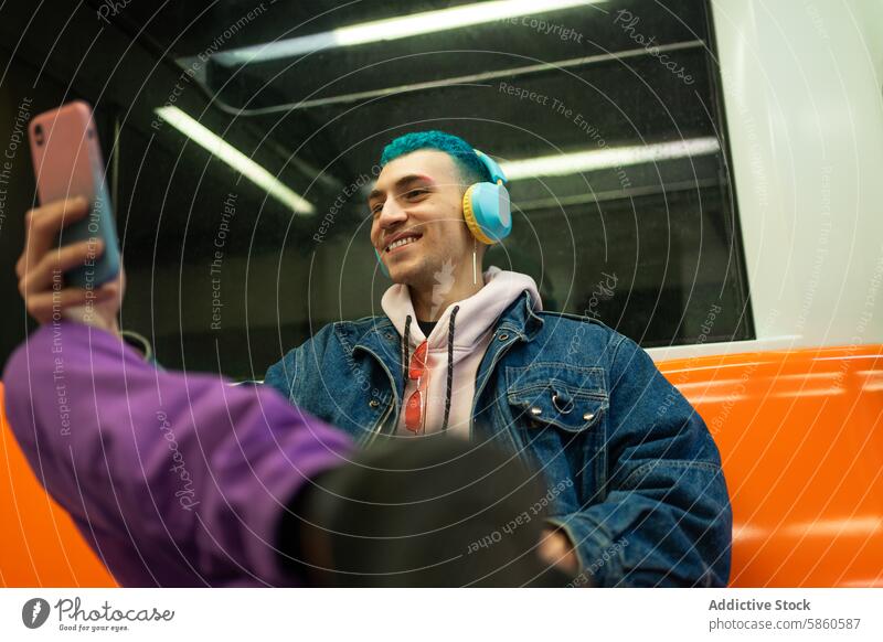 Young man enjoying music and social media on subway ride smartphone headphone travel transportation youth technology commuting casual jacket denim blue hair