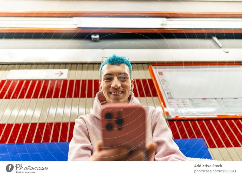 Young man with blue hair using smartphone in subway station young selfie cheerful colorful pattern background urban transport commuter travel technology mobile