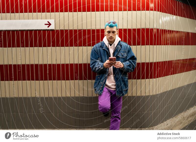 Young man using smartphone in a subway station style fashion urban city technology communication denim jacket colorful hair tile wall trendy young adult male