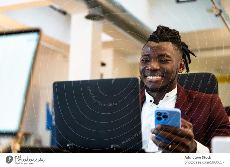 Young professional smiling using smartphone and laptop man young black office modern stylish blazer red multitasking digital connectivity corporate world