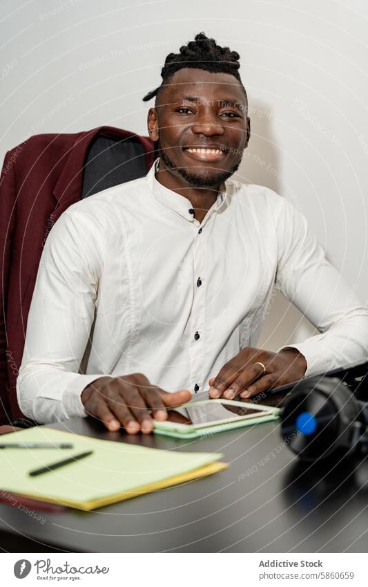 Smiling young businessman working at desk in office smiling white shirt cheerful professional workspace modern corporate technology tablet notebook headphones