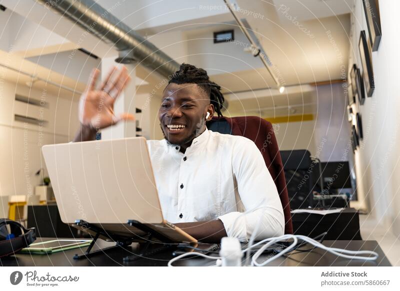 Cheerful man waving during a video call on laptop happy office workspace technology internet communication smiling computer desk modern casual professional