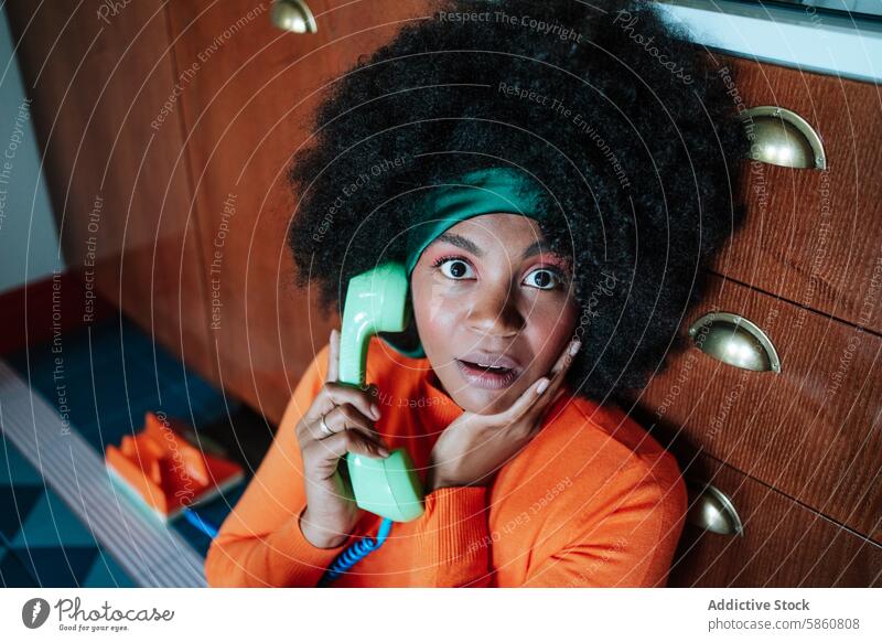 Surprised Black African american woman talking on retro phone in vintage style kitchen black afro surprised 1950s telephone orange green headband gaze housewife