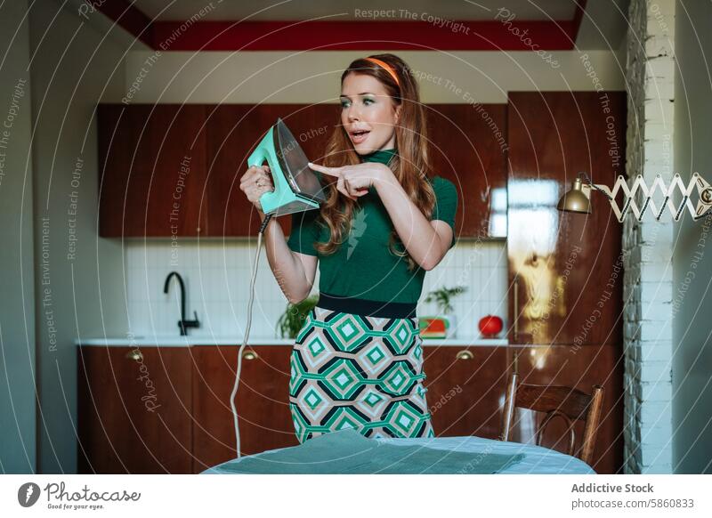 Woman in retro kitchen playfully pointing at iron woman 1950s vintage steam iron housewife feminine daily chore attire dressed channeling vibe situation styled